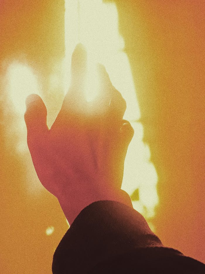 Crop anonymous person reaching out hand to flame during fire in orange light
